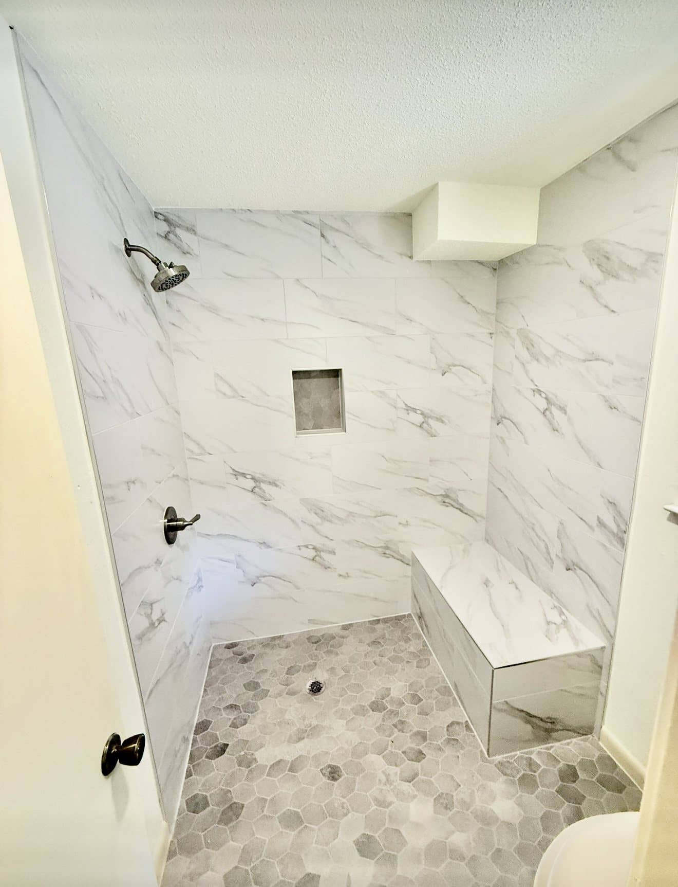 A finished Rhino Renovations marble shower with a built-in bench and clear-glass enclosure.